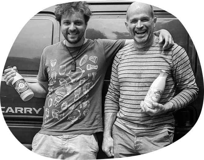 A photo of Joshua Coppersmith-Heaven with his arm around John Turner. Both are smiling and holding bottles of oat milk.